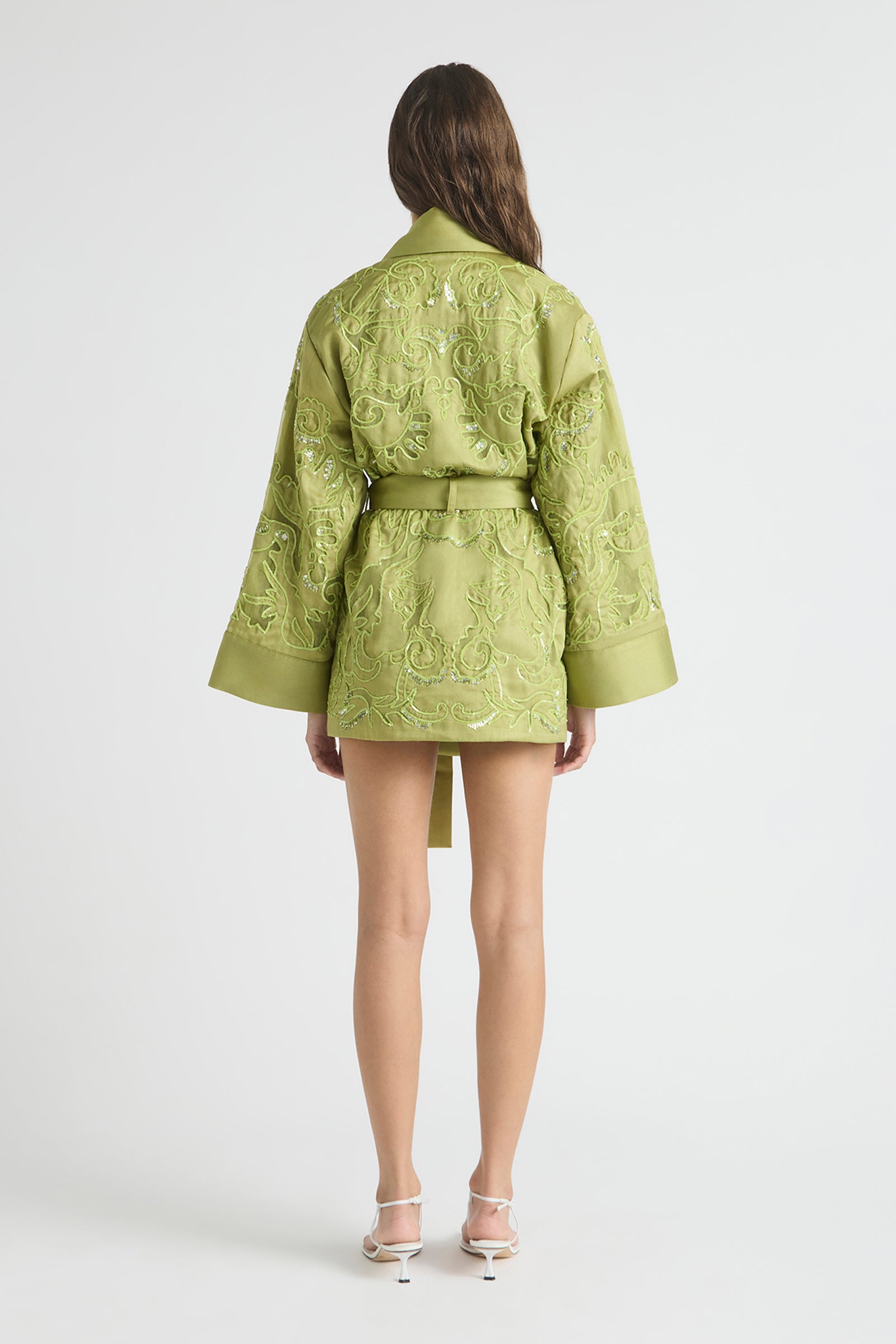 Person wearing a green embroidered jacket and shorts on a white background