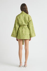 Person wearing a green embroidered jacket and shorts on a white background